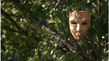 primo piano della chioma di un albero da cui si scorge una maschera